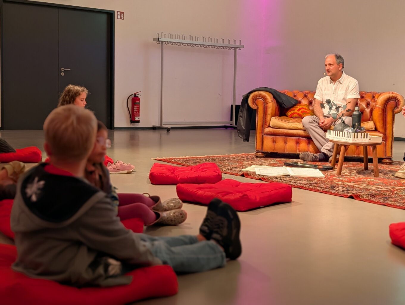 Kinder sitzen im Publikum und befragen einen Dirigenten, der auf einem Sofa sitzt.